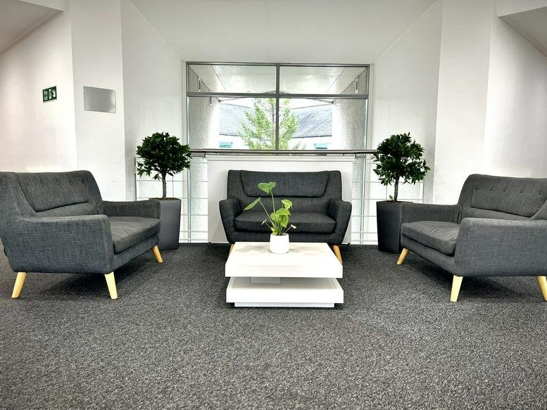 Spacious reception lounge with grey sofas and green plants at Castle Business Park, Lomond Court.