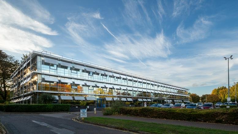 Wide exterior shot of a modern three-story office building with large windows under a blue sky.