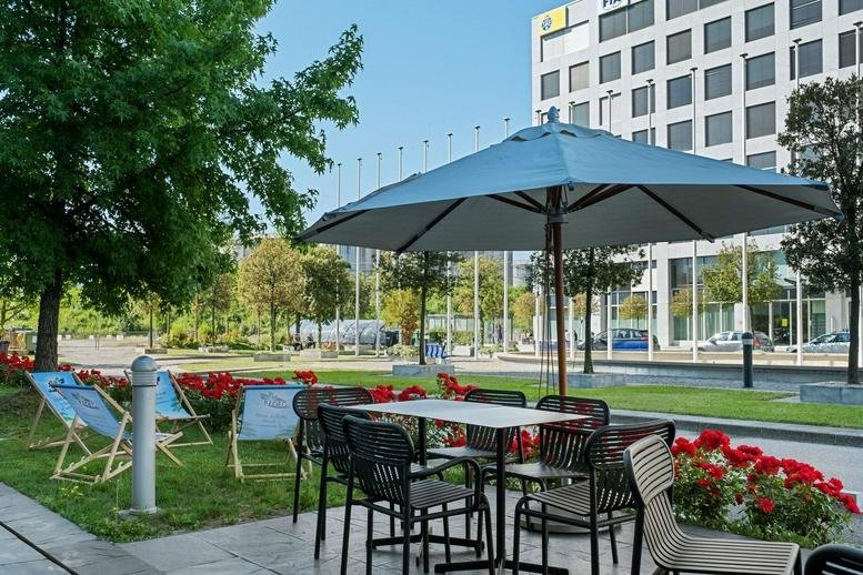 Sunny terrace at Chemin de blandonnet 8 with cafe tables, umbrellas, and deck chairs near the building.