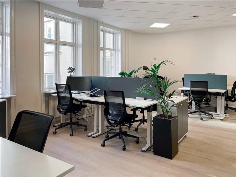 Open-plan workspace with white desks, black chairs, and large indoor plants.