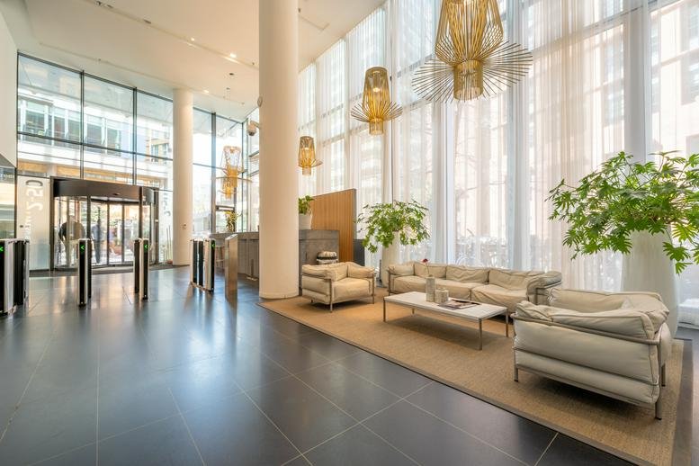 Bright, high-ceilinged lobby at Claude Debussylaan 10 with glass walls and contemporary seating.