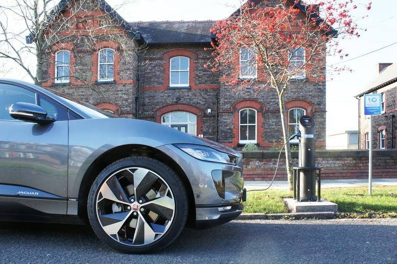 Stone building exterior with red brick accents and a grey car parked at an electric vehicle charging station.