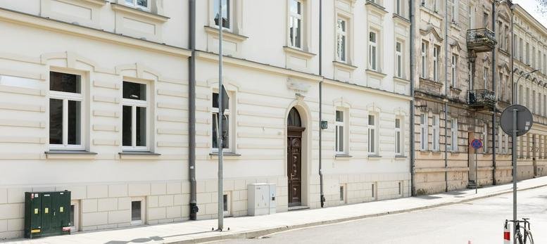 Bright street view showing the classic white building facade and entrance of Cluster Stare Podgórze.