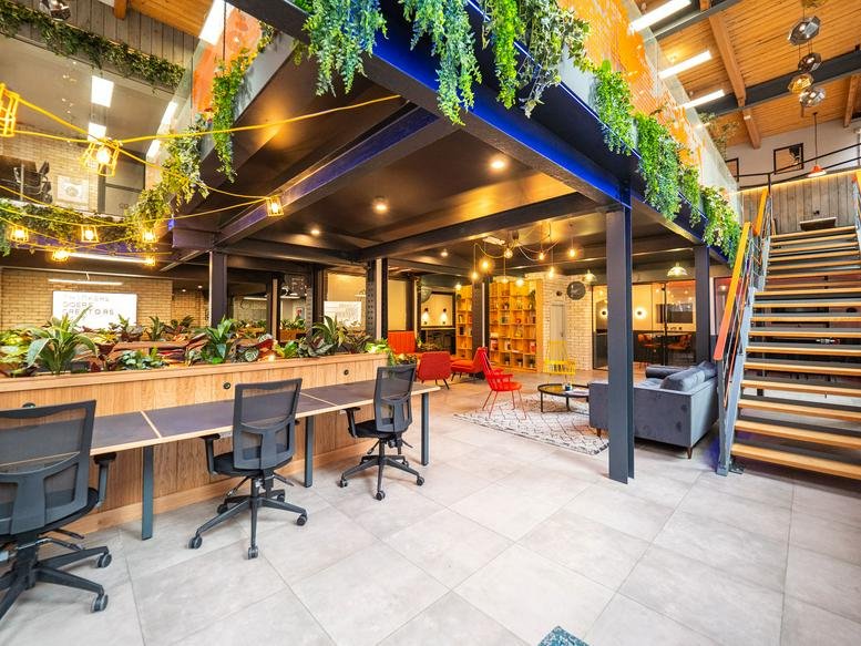 Spacious interior lobby of Colony Cowork, Jactin House with high ceilings, exposed beams, and hanging greenery.