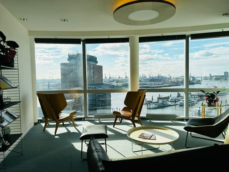 Sunlit communal lounge with modern armchairs and panoramic harbor views.