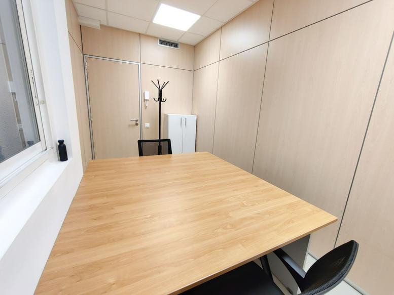 Interior office room with a large light wood desk, wall-mounted coat rack, and minimalist decor.