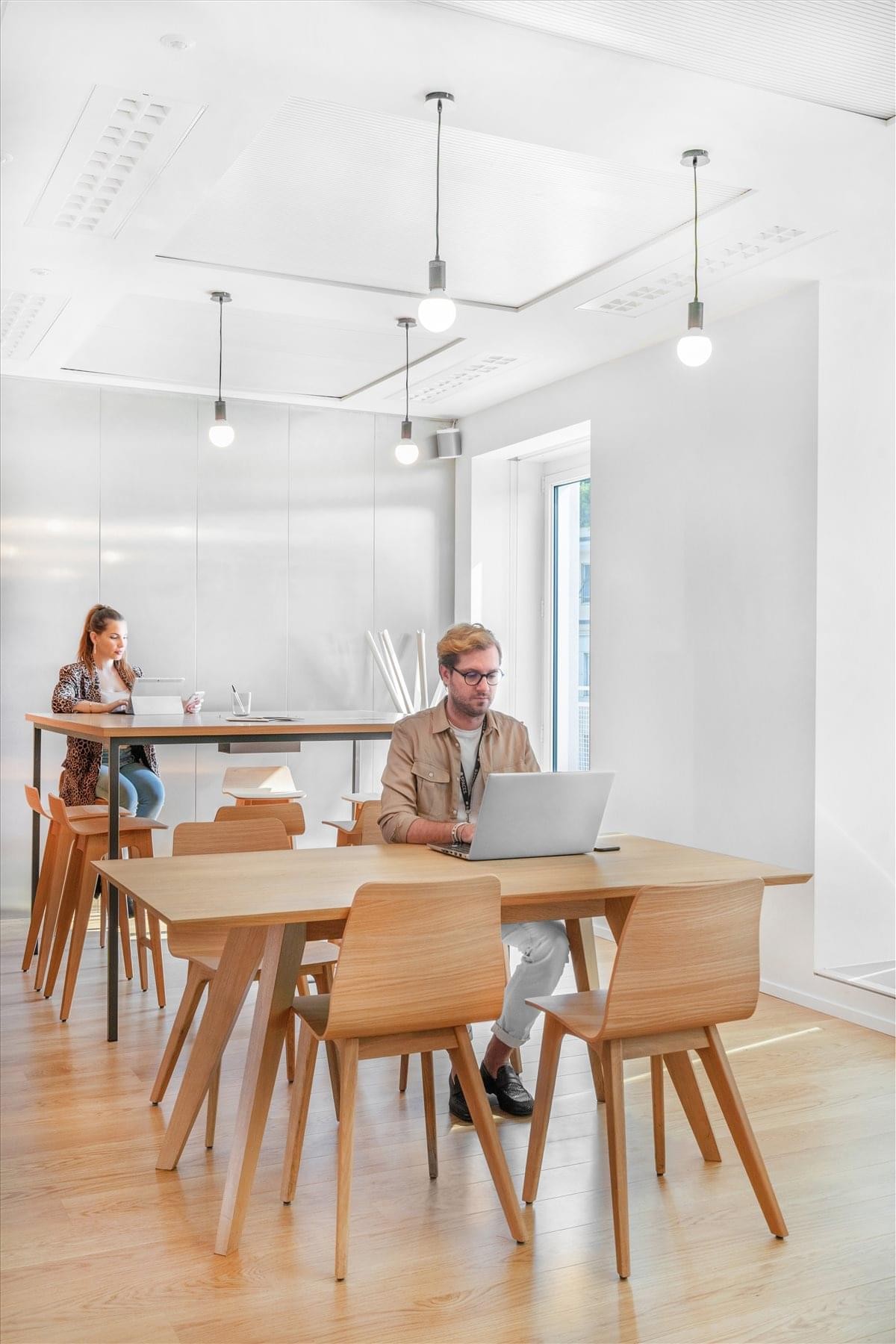 Bright, open-plan lobby at Corso Europa 15 with wooden tables, designer chairs, and warm lighting.
