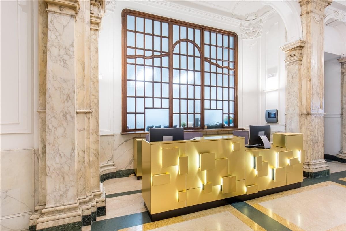 Grand lobby at Corso Valdocco 2 with a gold geometric reception desk and marble columns.