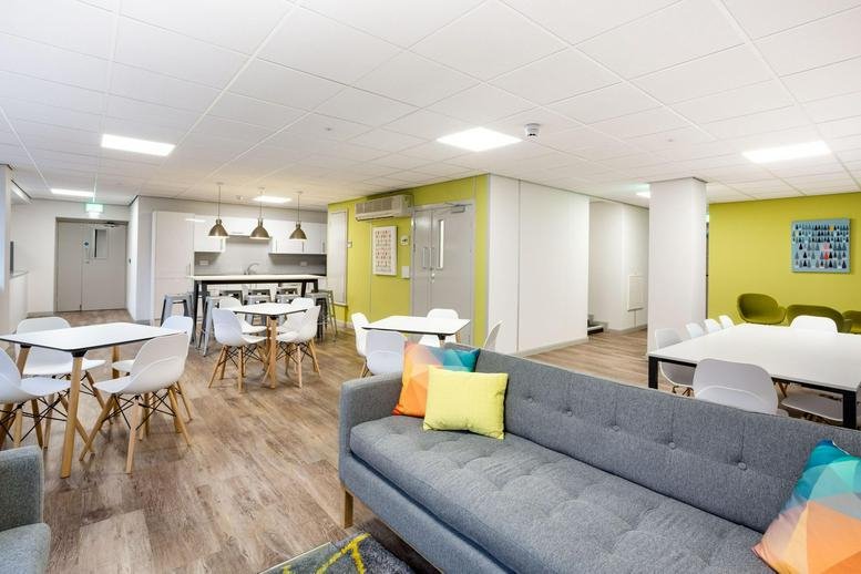 Vibrant communal breakout area with a grey sofa, colorful cushions, and a modern kitchen.