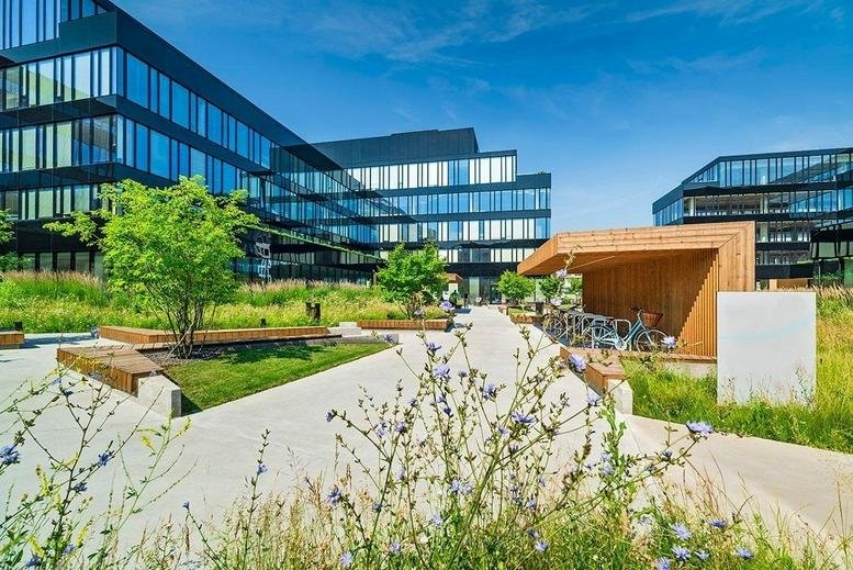 Exterior view of the modern glass-facade buildings at Cybernetyki 10, Warsaw, Poland with lush green landscaping.