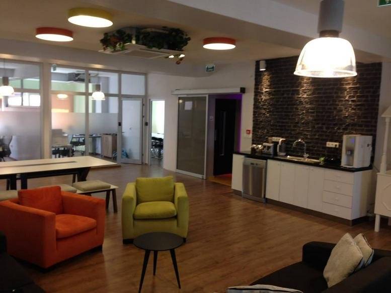 Spacious lounge and kitchenette at the Kamara DOME Building with colorful armchairs and a stone feature wall.