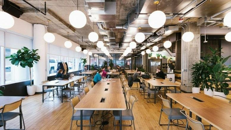 Spacious open-plan coworking area with long wooden tables and globe pendant lighting.
