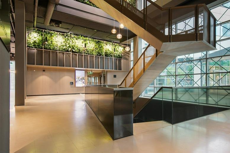 Bright multi-story lobby at De Entree 201 featuring a grand staircase and living wall.