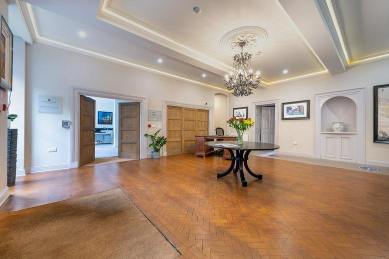 Bright reception area with polished wood floors, a central round table, and a crystal chandelier.