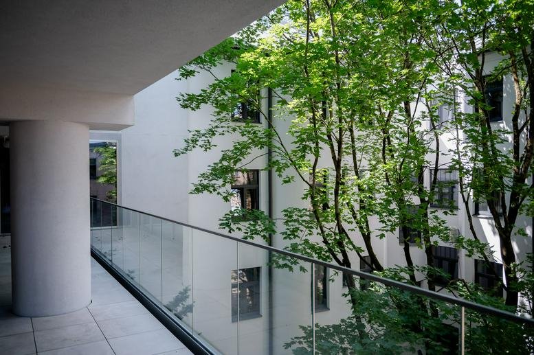 Exterior view of the white facade with large windows and lush green trees at Dzirnavu Lela 67, 5th floor, Riga.