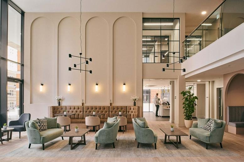 Spacious, high-ceilinged lounge at Eleven Brindleyplace with arched wall features and sage green velvet sofas.