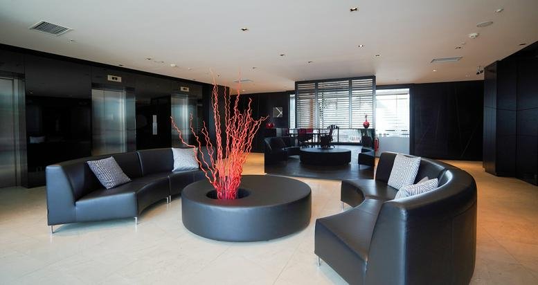 Spacious reception lounge at Exen Residence with curved black leather sofas and a vibrant red branch center piece.