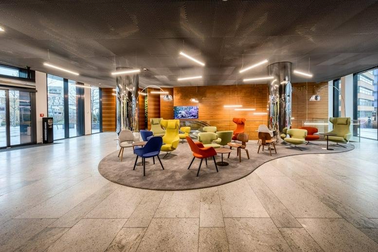 Spacious modern lobby with colorful armchairs on a wavy rug and chrome pillars.