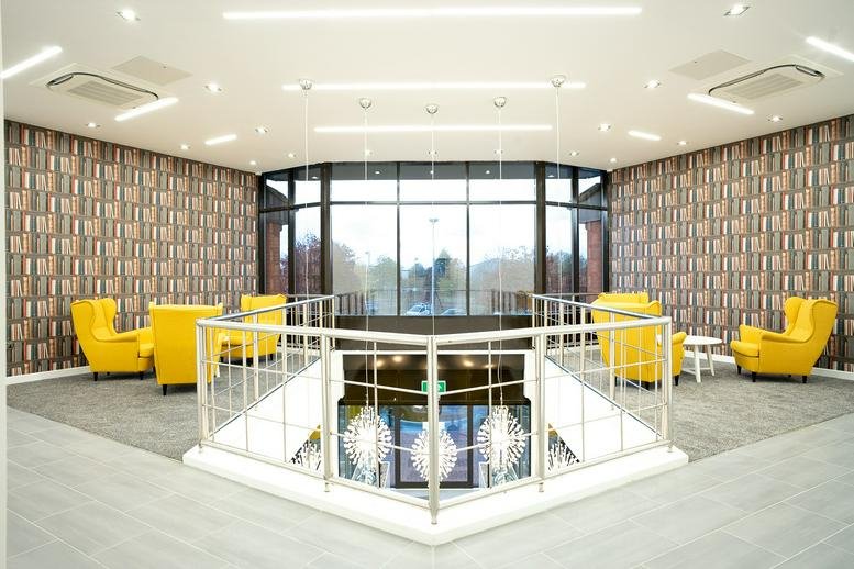 Foundry House lounge area with yellow wingback chairs and unique bookshelf-print wallpaper.