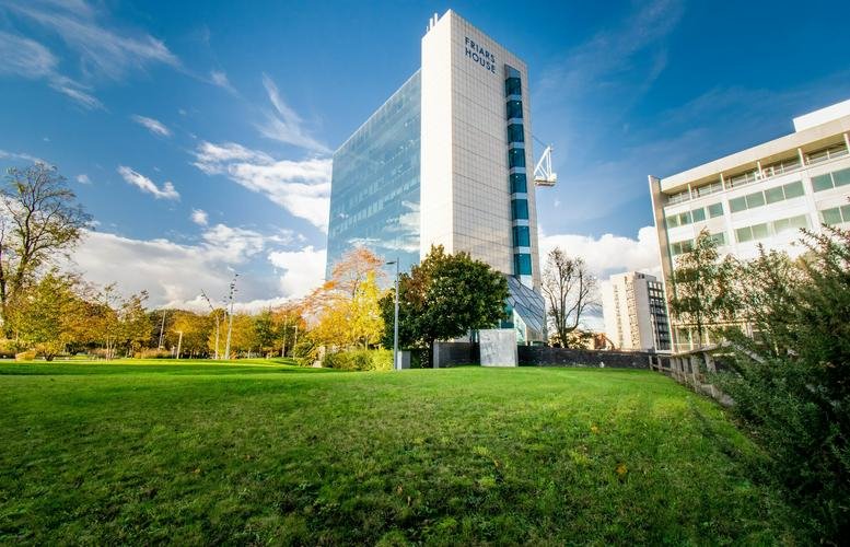 Exterior view of Friars House, a modern high-rise office building next to a green park.