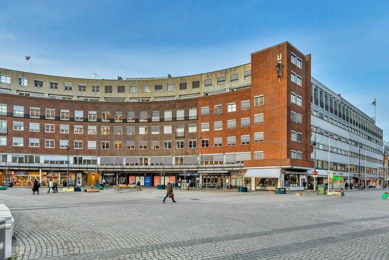 Curved brick facade of the Fridtjof Nansenplass 4 building overlooking a stone plaza.