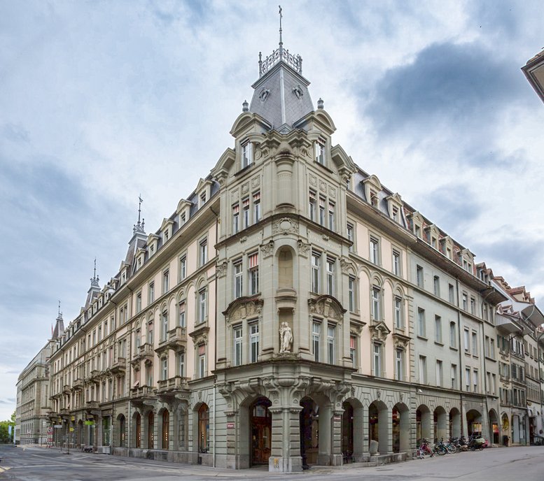 Exterior view of the historic stone building at Genfergasse 11, Bern, Switzerland featuring ornate corner turrets.