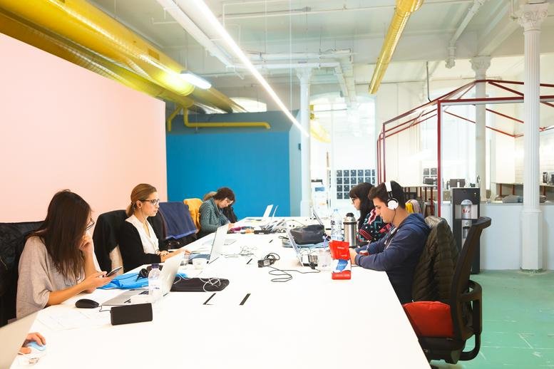 Spacious communal coworking space at Gran Via de les Corts Catalanes 672, Barcelona with colorful walls and yellow pipes.