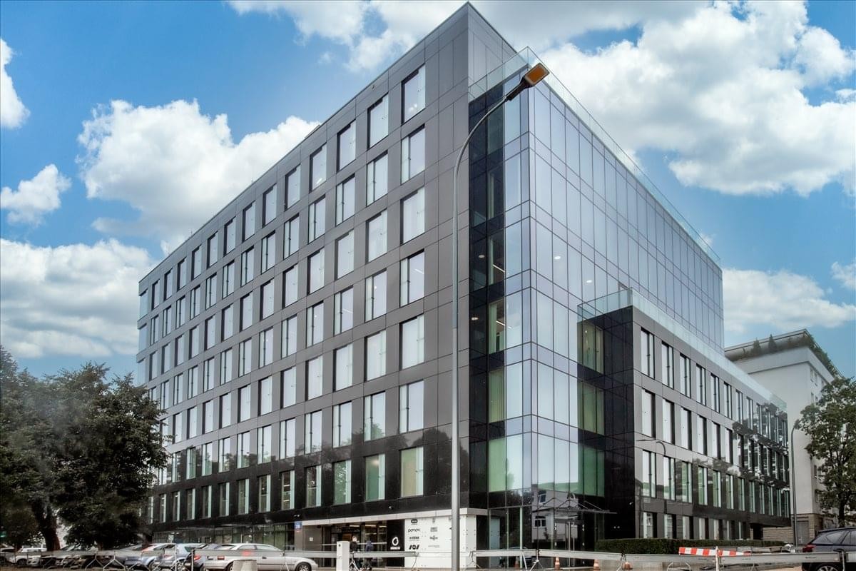 Modern glass and stone exterior of the Grojecka Offices building under a blue sky.