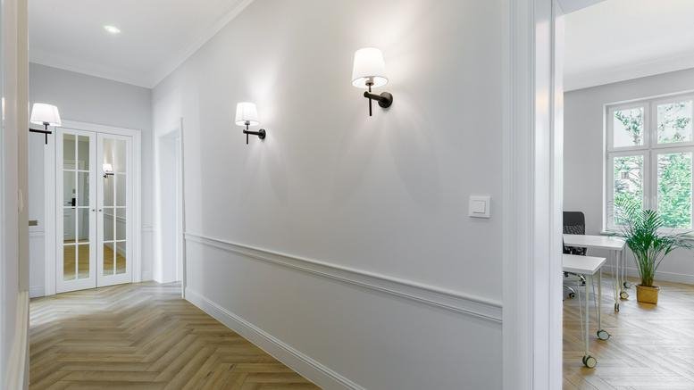 Bright hallway at Grunwaldzka 26/3 with decorative wall molding, wall sconces, and chevron wood flooring.