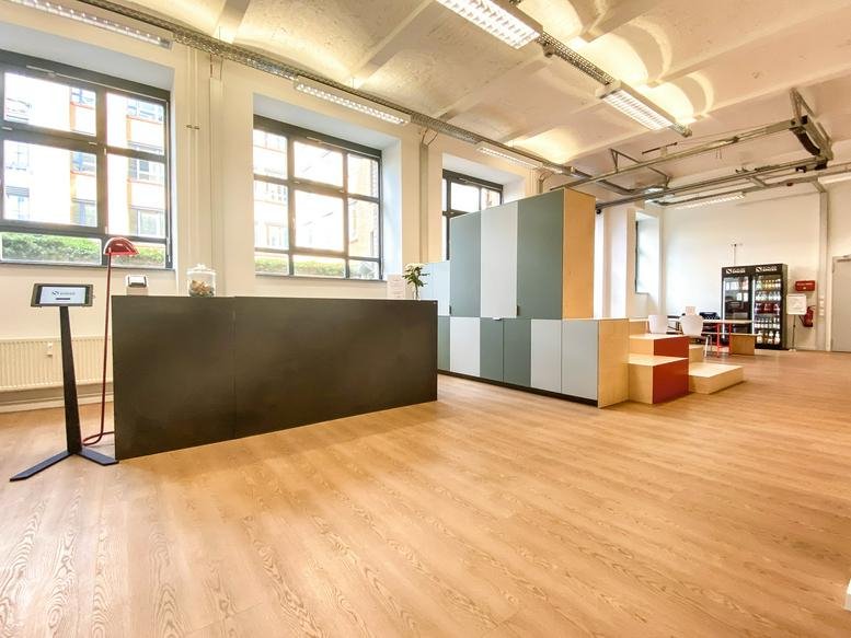Spacious reception area at Comeniushof Fabrik with a dark front desk and warm wood flooring.