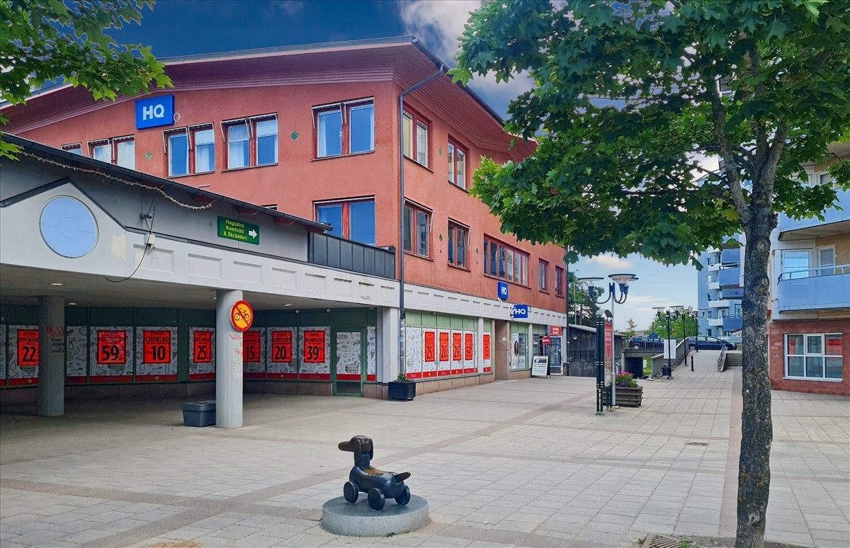 Exterior view of the red brick building at Hagsätra Torg 13 with retail shops on the ground floor.