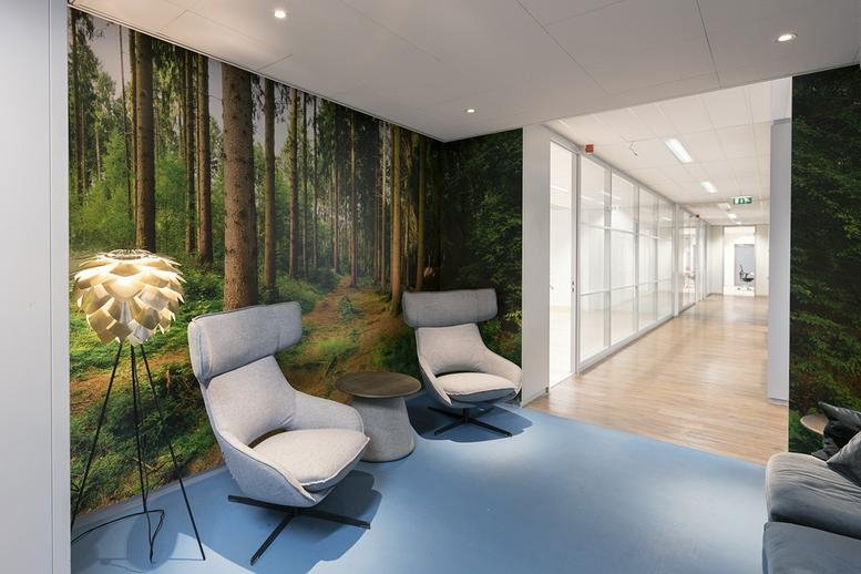 Modern lounge area at Handelsweg 53 with forest-themed wall mural and grey wingback chairs.