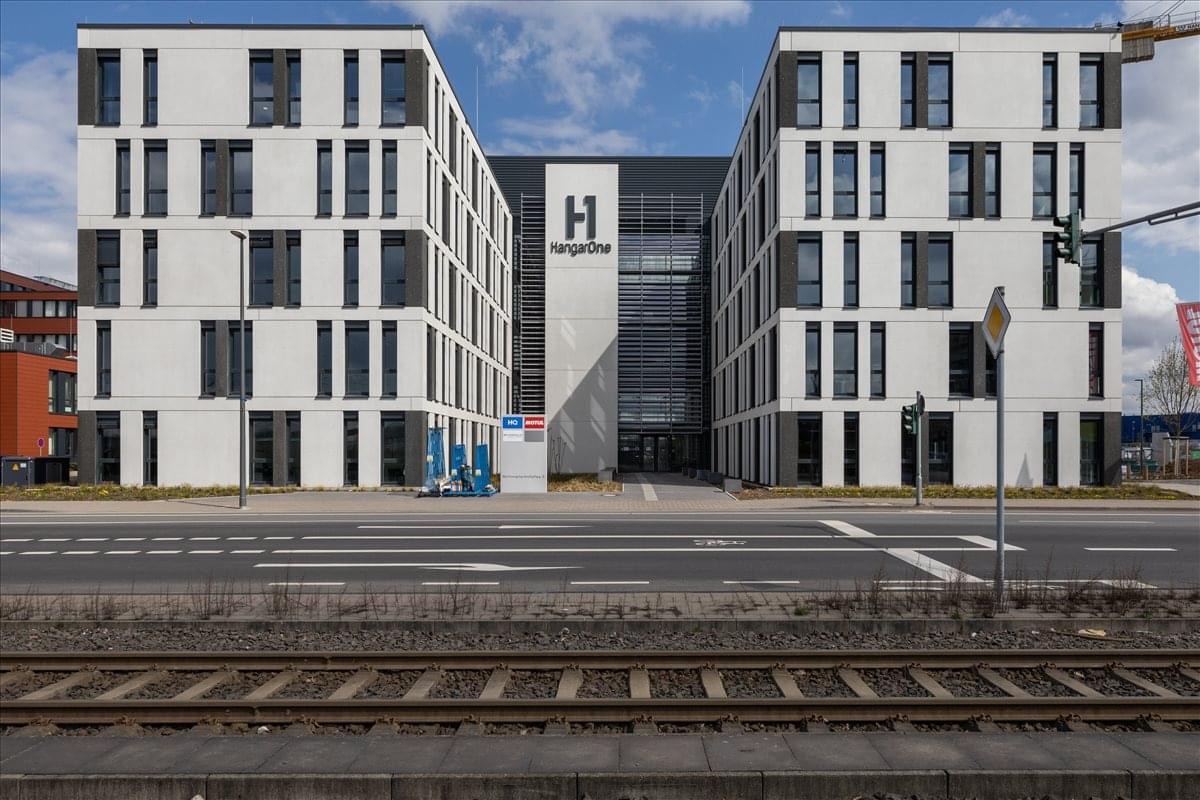 Exterior view of the modern white HangarOne building with a central glass entrance.