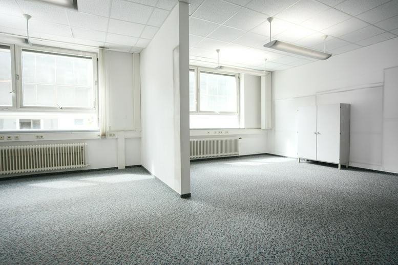 Spacious open-plan office divided by a partial wall with large windows.