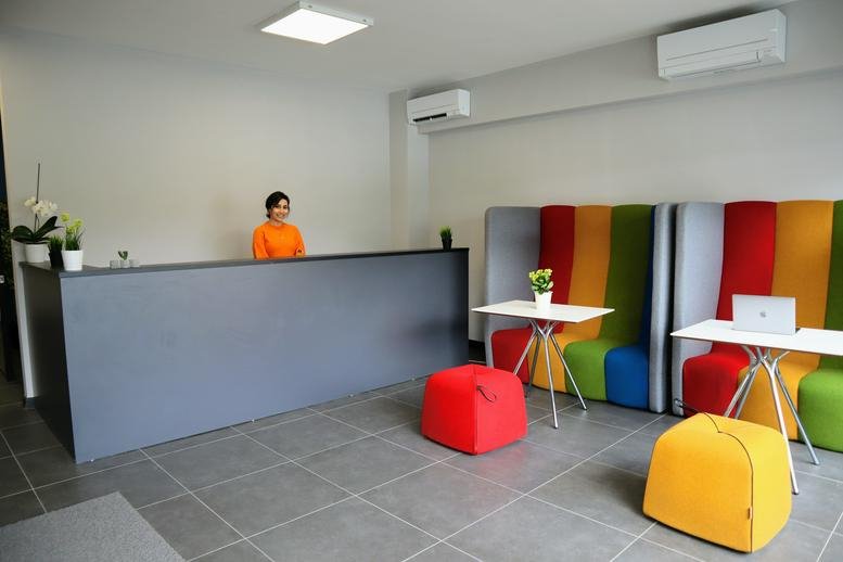 Reception area with grey desk, orange-shirted receptionist, and vibrant multi-colored bench seating.