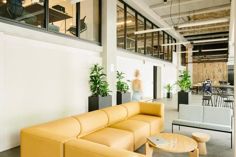 Spacious communal area featuring a long yellow sectional sofa and indoor plants.