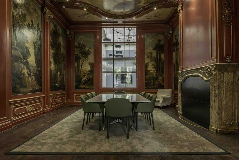 Formal meeting room featuring classical wall murals, dark wood paneling, and a large fireplace.