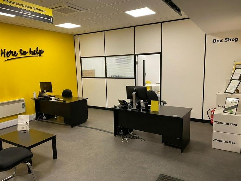 Reception area featuring a bright yellow feature wall, two black desks, and a box shop display.