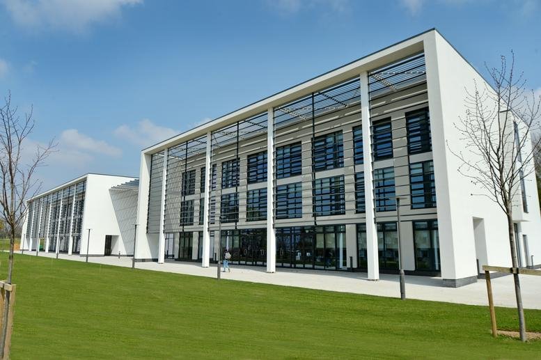 Wide exterior shot of the three-story white office building with extensive glazing and a green lawn.