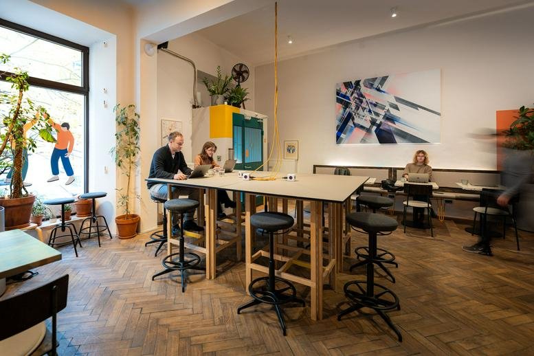Spacious coworking area with high-top wooden tables, herringbone floors, and natural light.