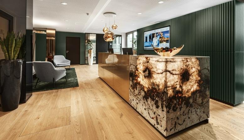 Modern reception area at Königstrasse 38 with a backlit stone desk and dark green textured walls.