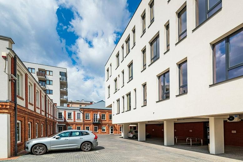Exterior view of the white and brick facade at Kaleńska 5, Warsaw, Poland with a parked car.