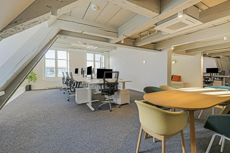 Bright attic workspace with timber beams and multiple desks.