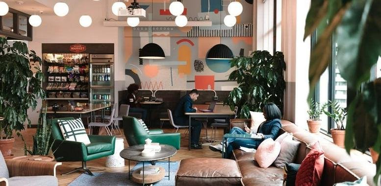 Spacious, vibrant communal lounge at Kings Place, 90 York Way with colorful murals, plants, and mid-century furniture.