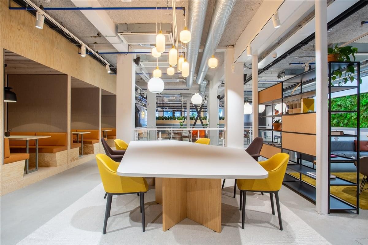 Large shared workspace at Kristian Augusts Gate 13 with diverse seating and hanging globe lights.