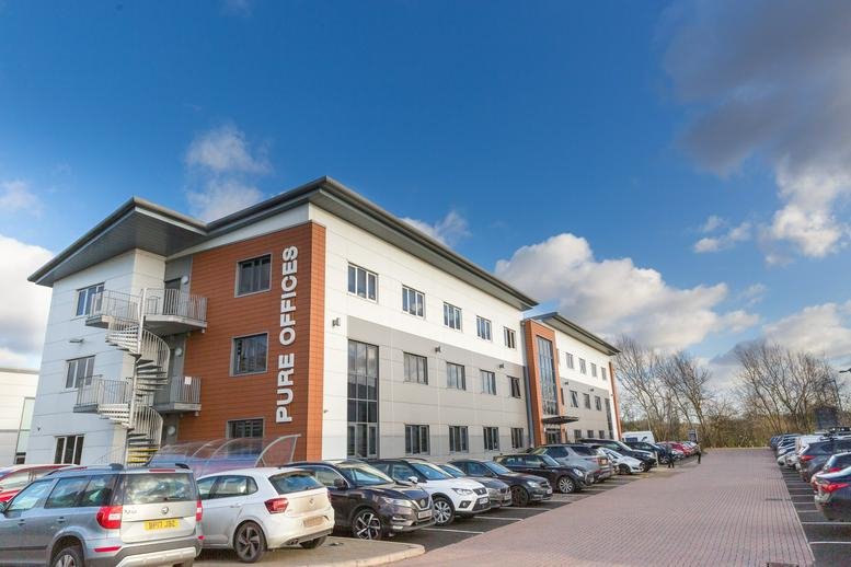 Wide exterior shot of the commercial office building and parking lot under a blue sky.