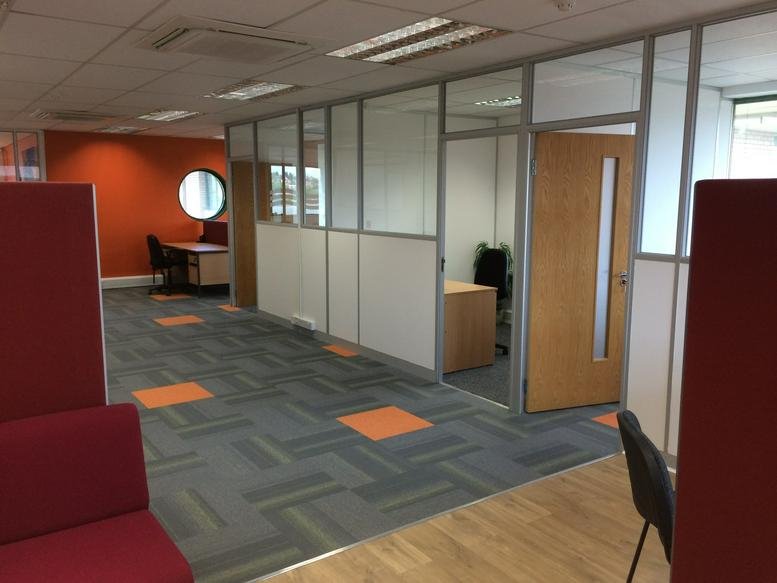 Open-plan office area with glass partitions and orange accents.