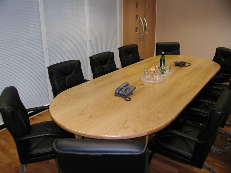 Professional boardroom featuring a large oval wooden table and black leather chairs.