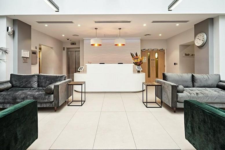 Bright, modern reception area at Longcroft House featuring white desks and velvet sofas.