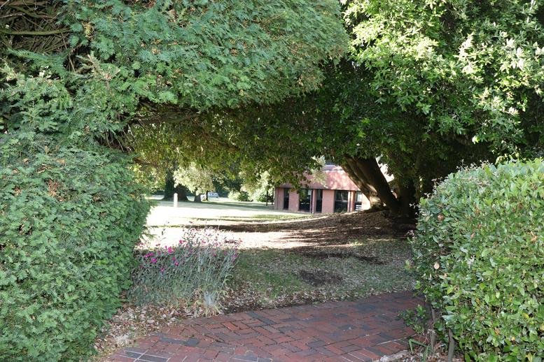 Lush green lawn and mature trees surrounding a brick outbuilding.